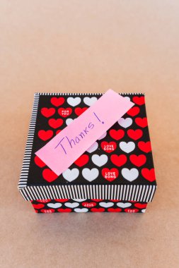 Teşekkür notu, kırmızı ve beyaz kalpli bir hediye kutusunun arka planına sahip mavi kalemle yazılmış.