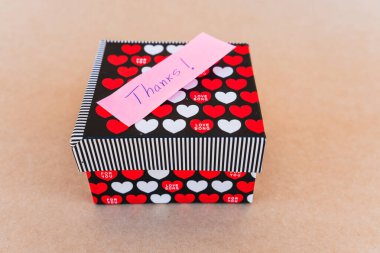 Teşekkür notu, kırmızı ve beyaz kalpli bir hediye kutusunun arka planına sahip mavi kalemle yazılmış.