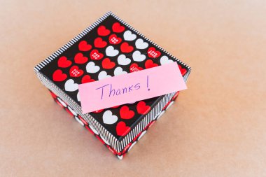 Teşekkür notu, kırmızı ve beyaz kalpli bir hediye kutusunun arka planına sahip mavi kalemle yazılmış.