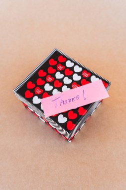 Teşekkür notu, kırmızı ve beyaz kalpli bir hediye kutusunun arka planına sahip mavi kalemle yazılmış.