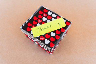 Teşekkür notu, kırmızı ve beyaz kalpli bir hediye kutusunun arka planına sahip mavi kalemle yazılmış.