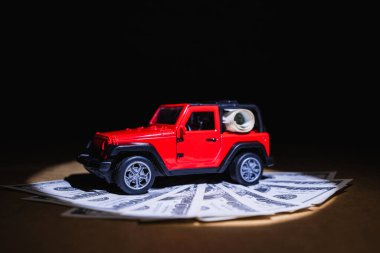 Siyah arka planı olan arabayı almak için biriktirilmiş yüz dolarlık banknotlar üzerinde kırmızı bir cip.