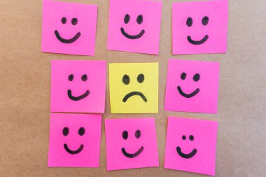 Üzücü yüz, renkli kağıda çizilmiş mutlu yüzlerle çevrili. Siyah işaretli, tek tip, sağlam bir arkaplanı var.