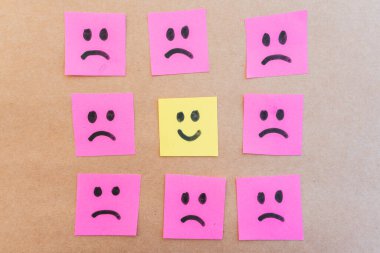 Renkli kağıda çizilmiş üzgün yüzlerle çevrili mutlu bir yüz.