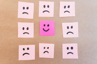 Renkli kağıda çizilmiş üzgün yüzlerle çevrili mutlu bir yüz.