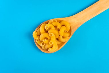 Mavi bir yüzey üzerinde ahşap bir kaşıkta erişteler ve mutlu ve hüzünlü ifadeleri olan bir doğrama tahtası.