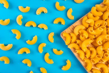 Mavi bir yüzey üzerinde ahşap bir kaşıkta erişteler ve mutlu ve hüzünlü ifadeleri olan bir doğrama tahtası.