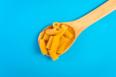 Mavi bir yüzey üzerinde ahşap bir kaşıkta erişteler ve mutlu ve hüzünlü ifadeleri olan bir doğrama tahtası.