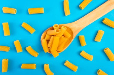 Mavi bir yüzey üzerinde ahşap bir kaşıkta erişteler ve mutlu ve hüzünlü ifadeleri olan bir doğrama tahtası.