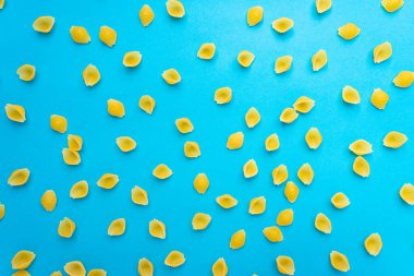 Mavi bir yüzey üzerinde ahşap bir kaşıkta erişteler ve mutlu ve hüzünlü ifadeleri olan bir doğrama tahtası.