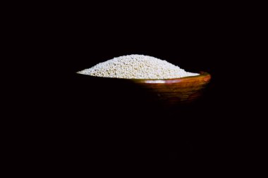 Eski bir seramik kasede renkli bir kumaşın üzerinde siyah bir kaşık olan kinoa.