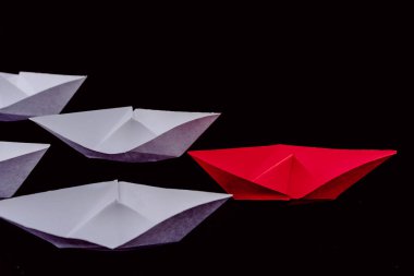 Kağıt tekneler liderliği ve siyah arka planlı beyaz ve kırmızı giyen kalabalığın önünde durmak..