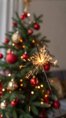 A lit sparkler in front of a blurred Christmas tree with red and gold ornaments.. AI generated photo. 4K. HD Image Background clipart