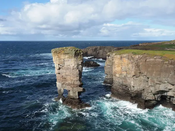 Yesnaby Şatosu deniz yığınları ve uçurumlar. Orkney adaları. İskoçya. Muhteşem bir Kızıl Kum Taşı kıyı uçurumu manzarası. Bu bölge, iki ayaklı bir deniz yığını olan Yesnaby Kalesi sayesinde dağcılar arasında popülerdir..