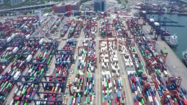 Endüstriyel bir konteynır limanının havadan görünüşü - hareketli bir deniz merkezinin kapsamlı ve ayrıntılı perspektifi. Kamera, liman boyunca düzenli bir şekilde düzenlenmiş çeşitli canlı renklerde istiflenmiş nakliye konteynırlarının geniş bir düzenini yakalar..