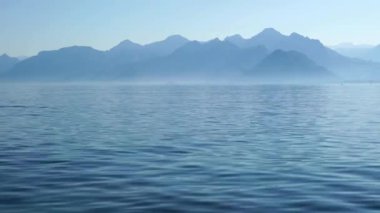 Sakin göl ve dağların puslu doğal manzarası. Huzur ve doğal güzelliğin birleştiği huzurlu ve ruhani bir manzara. Sis yavaşça suyun üzerinde sürükleniyor, yumuşak, rüya gibi bir ortam yaratıyor..