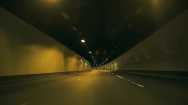 Gece Tüneli 'nde Sürüş Görüntüsü. Aydınlatılmış bir tünelden geçen gece yolculuğunun büyüleyici ve dinamik bir görüntüsü. Islak yüzeylerden veya parlak malzemelerden gelen ara sıra yansımalar hareket ve hız duygusunu arttırır..