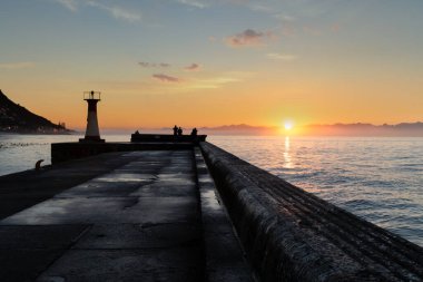 Siluetli deniz feneri ve insanlar gün doğumunda iskelede