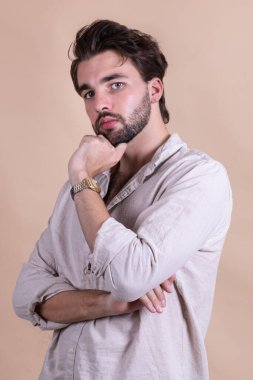 Studio shot of young handsome bearded man in shirt on beige studio background clipart