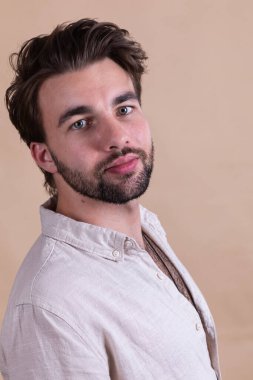Studio shot of young handsome bearded man in shirt on beige studio background clipart