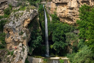 Bir şelale kayalık bir uçurumdan aşağı akıyor. Su berrak ve kayalar kahverengi. Huzurlu ve huzurlu bir sahne.