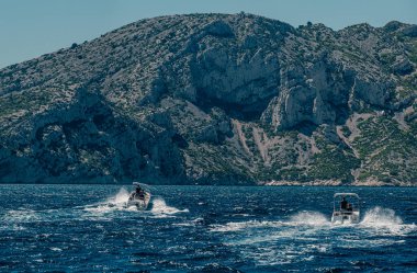 Sürat tekneleri açık bir gökyüzünün altında kayalık Calanques yakınlarında yarışıyor
