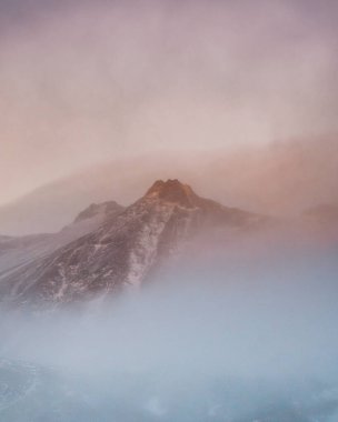 Güney İzlanda 'da gün batımında karla kaplı, puslu dağların kasvetli manzarası