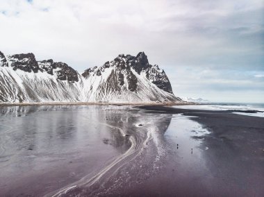 Karla kaplı Vestrahorn dağları güneydoğu İzlanda 'daki Stoksnes sahilindeki buzlu sulara yansıyor..