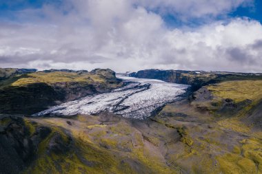 İzlanda 'daki Solheimajokull buzulunun havadan görünüşü, parlak yeşil yosun kaplı dağların, katı beyaz buzullarla çelişmesi.