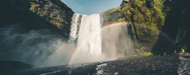 İzlanda 'daki Skogafoss şelalesinin yakından görüntüsü. Sis ve yemyeşil kayalıklar arasında canlı bir gökkuşağı var..