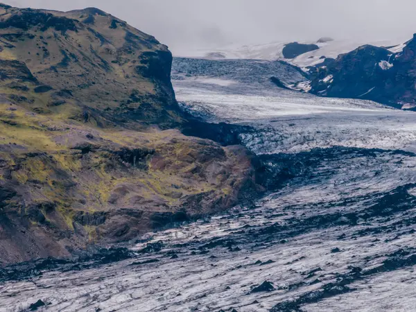 stock image Aerial view of Solheimajokull glacier in Iceland, featuring vibrant green moss-covered mountains contrasting with the stark white glacier