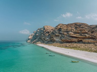 Pristine turquoise waters and stunning rock formations at Shoab Beach, Socotra, Yemen, with traditional boats anchored along the shore. clipart