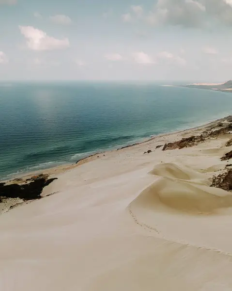 stock image Aerial view of Arher Beach in Socotra, Yemen, showcasing pristine white sand dunes meeting the turquoise waters of the Arabian Sea under a partly cloudy sky.