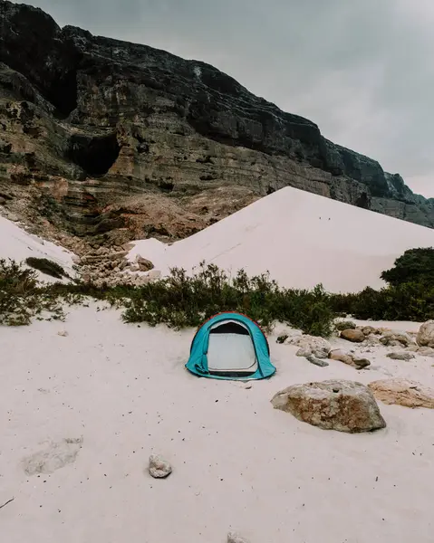 Socotra, Yemen 'deki Arher Sahili' nin beyaz kum tepelerine kurulmuş bir çadır. Arka planda bulutlu bir gökyüzünün altında dramatik tepeler var..