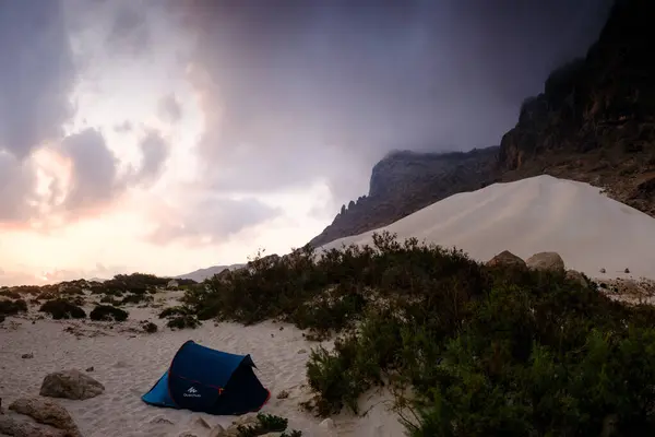 Arher Sahili, Socotra, Yemen 'de gün batımı manzarasında görkemli kum tepeleri ve engebeli dağlara karşı tek başına bir kamp çadırına ev sahipliği yapıyor..