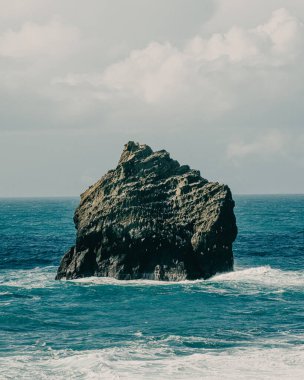 Reykjanes Yarımadası, İzlanda 'daki Karlinn kuş uçurumunun yakın görüntüsü. Etrafı okyanus dalgaları ve yumuşak bulutlu gökyüzünün altındaki canlı mavi sularla çevrili.