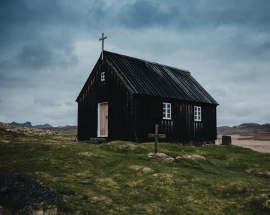 İzlanda 'nın Reykjanes Yarımadası' ndaki tarihi siyah ahşap kilise Krysuvikurkirkja 'nın yakın çekim alanı dramatik bulutlu bir gökyüzüne ve uzak volkanik manzaraya karşı kurulmuştur.
