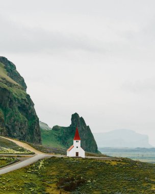 Vikurkirkja church in Vik, South Iceland, surrounded by dramatic cliffs and lush green fields clipart