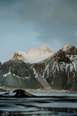 Vestrahorn dağını aydınlatan altın saat ışığı ve İzlanda 'nın güneydoğusundaki siyah kumsal plajını yansıtıyor.