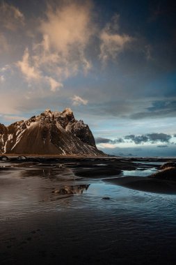 Golden hour light illuminating Vestrahorn mountain and reflections on the black sand beach in southeast Iceland clipart