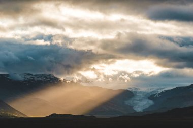 Güneş ışınları Güney İzlanda 'daki Hoffellsjokull buzulu üzerinde bulutların arasından doğuyor..