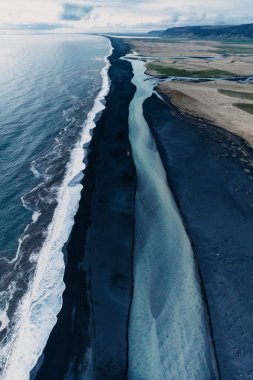 Güney İzlanda 'da siyah bir kumsalda okyanusla birleşen buzul nehrinin havadan görünüşü.