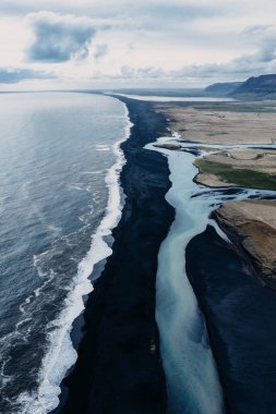 Güney İzlanda 'da siyah bir kumsalda okyanusla birleşen buzul nehrinin havadan görünüşü.