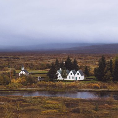 İzlanda 'daki Thingvellir Milli Parkı manzarası. Tarihi kilise, sonbahar yeşilliği ve sakin nehir manzarası.