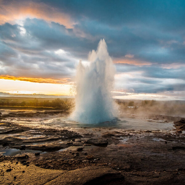 Strokkur geysir erupting with hot water and steam at sunrise in south Iceland