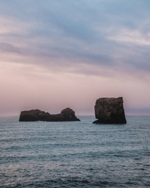 Dyrholaey, Güney İzlanda 'da parlak bir gökyüzünün altında kaya oluşumlarıyla dramatik deniz manzarası.