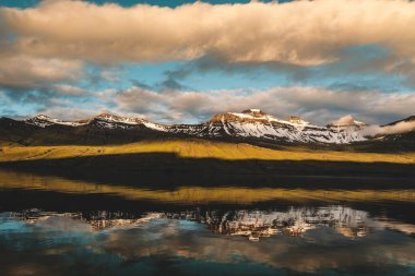 Karlı dağların üzerinde huzurlu bir gün doğumu ve İzlanda, Faşkrudsfjordur 'da sakin bir fiyort