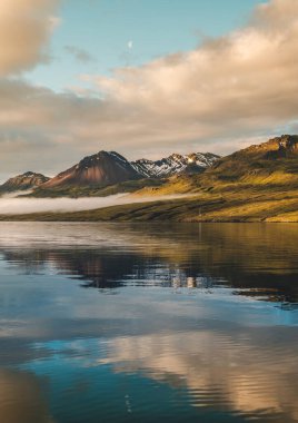 Karlı dağların üzerinde huzurlu bir gün doğumu ve İzlanda, Faşkrudsfjordur 'da sakin bir fiyort