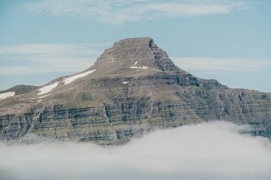 Svartafjall dağının katmanlı zirvesi Reydafjordur, Doğu İzlanda kıyı bulutlarının üzerinde yükseliyor.