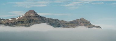 Svartafjall dağının katmanlı zirvesi Reydafjordur, Doğu İzlanda kıyı bulutlarının üzerinde yükseliyor.